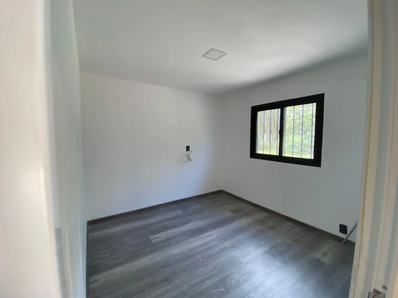 Dormitorio con piso símil madera y ventana con reja